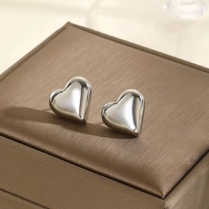 Minimalist silver heart stud earrings with polished geometric finish on a textured surface