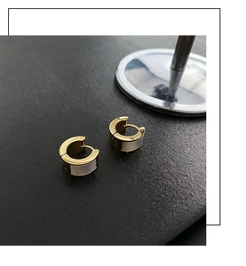 Close-up of gold titanium huggie earrings with white mother-of-pearl inlay on black leather