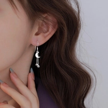Detail of silver S-shaped wave tassel earring with moon charm on model's ear