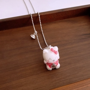Detail of white flocked kitten pendant with pink bow and silver planet charms on chain