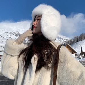 Close-up of white plush earflap hat and beige faux fur coat against snowy mountains