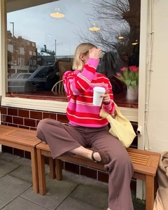 Outdoor shot of a pink and red striped polo knit sweater with brown wide-leg pants