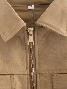 Détail macro du col en sergé de coton kaki avec fermeture éclair dorée et étiquette S