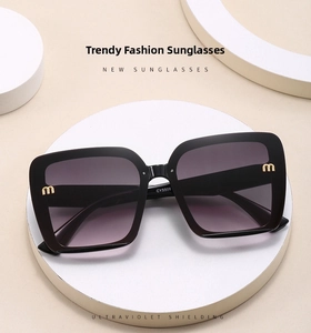 Detail of black oversized square sunglasses with gold logo on a white pedestal stand
