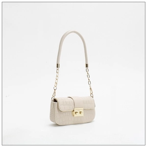 Close-up of crocodile pattern texture with gold metal clasp and chain on cream bag