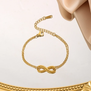 Golden double-layer infinity charm bracelet in stainless steel on a mirrored tray