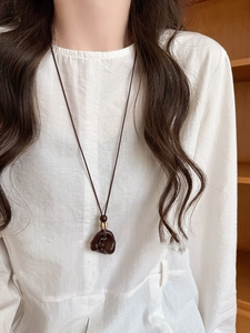 Close-up of irregular wood resin pendant necklace with gold bead on white linen shirt