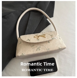 Détail d'un sac baguette en paille avec broderie florale et nœud doré élégant