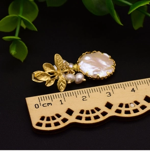 Macro shot of Baroque pearl drop earrings with golden leaves and size reference