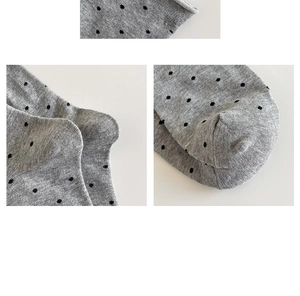 Close-up detail of grey knitted crew socks featuring black polka dots and rolled cuff edges