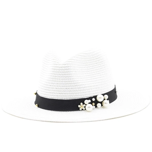 Detail of white straw sun hat featuring black ribbon with pearls and golden floral charms