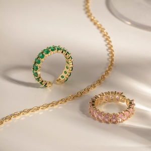Gold open rings with oval emerald green and pink zircons on a sunny minimalist background