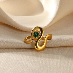 Detailed view of a gold wavy ring featuring a green gemstone on soft silk fabric