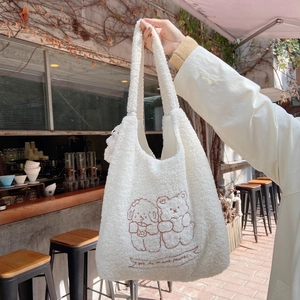 Close-up of plush white tote bag featuring brown teddy bear embroidery and long handles