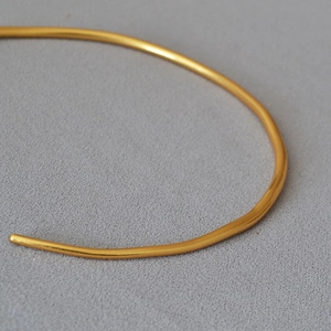 Macro detail of minimalist gold-plated brass choker with polished curved metallic texture