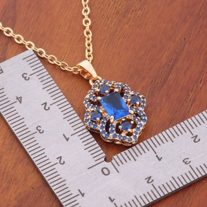 Gold rhombus pendant with blue zircon stones on wood background showing size measurement