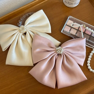 Detail of beige and pink oversized satin bow hair clips with pearl camellia centers