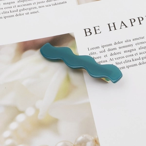 Macro shot of wavy emerald acetate hair clip showing the smooth resin texture and shape
