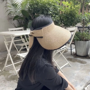 Detail of wide brim straw sun hat with dark bow trim and woven texture in outdoor setting