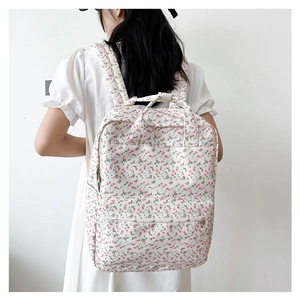 Floral canvas backpack with pink flower patterns worn by model against a white wall