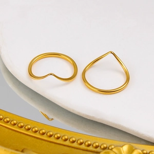 Close-up of two stackable golden V-shaped titanium steel rings on white marble stone