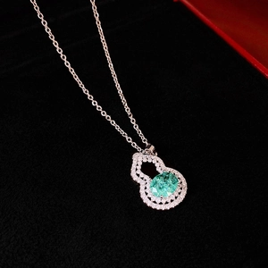 Macro shot of silver gourd pendant with green gemstone and pavé diamonds on black velvet