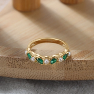 Detail eines Vintage-Goldrings mit grünem Edelstein und weißer Perle auf Holzgrundlage