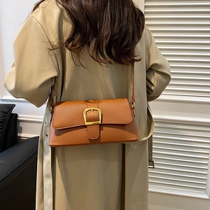 Close-up of brown leather shoulder bag with gold buckle on a model in a minimalist room