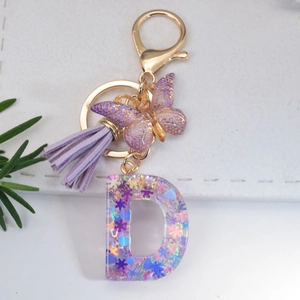 Detail of purple letter D keychain with glitter resin, suede tassel and golden butterfly