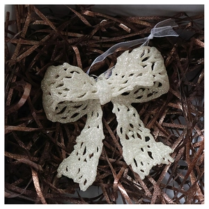 Close-up of champagne sequin bow ornament with hollow lace pattern in a gift box