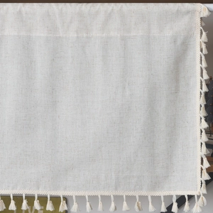Close-up of beige cotton linen cafe curtain with textured weave and fringe tassels