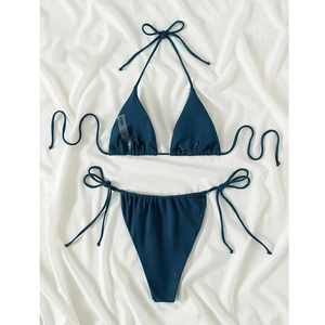 Flat lay detail of dark teal triangle bikini set with side-tie bottoms on textured fabric
