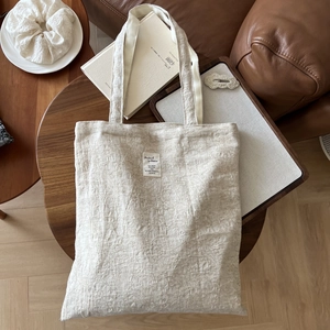 Detail of cream canvas tote bag with textured fabric and fabric label on a wooden table