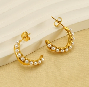 Detail of gold C-shaped hoop earrings with embedded white pearls on textured stone