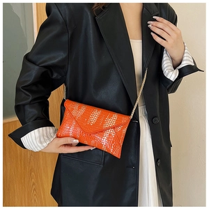 Detail view of orange crocodile texture handbag with glossy finish and gold chain strap