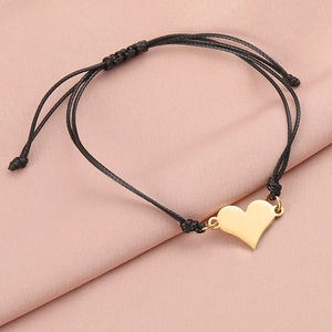 Detail of adjustable black woven bracelet with polished gold heart pendant on pink silk