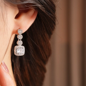 Close-up of silver stud earring with square and round white cubic zirconia on a female ear