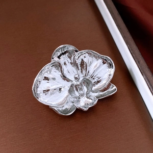 Detailed close-up of a silver orchid flower brooch with a smooth polished mirror finish