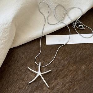 Close-up of a silver starfish pendant on a snake chain over a dark wooden texture