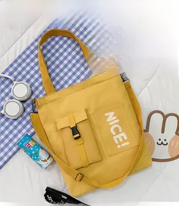 Top view of yellow canvas tote bag with NICE print and buckle pocket on white mattress