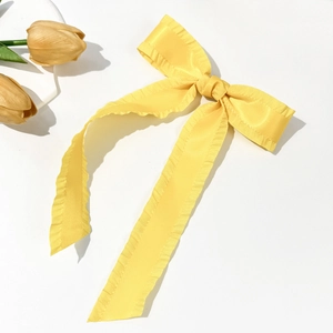 Detail of yellow satin hair clip with ruffled edges and elegant long ribbons