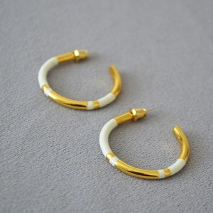 Macro view of gold-plated C-shaped earrings featuring cream white enamel and metal panels