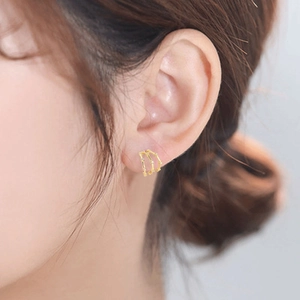 Close-up of three-tier gold-plated C-shaped earrings with diamonds on model ear