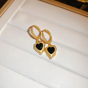 Close-up of matte gold heart drop earrings with black gemstone inlay on a jewelry tray