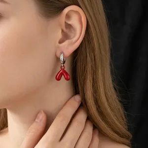 Ancora red heart drop earrings with silver needles worn by model on black background