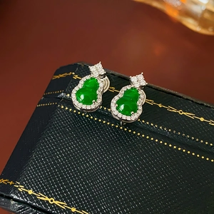 Macro shot of green jade gourd earrings with silver and zircon accents on blue case