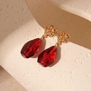 Detail of red teardrop resin pendant with golden rose stud and multifaceted crystal texture
