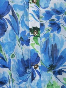 Detailed close-up of blue floral textile pattern and three brass buttons on shirt placket