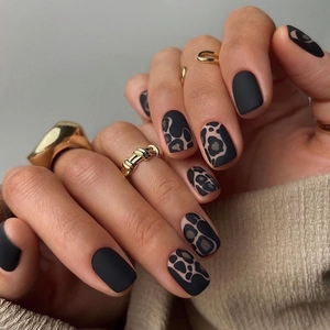 Matte black and leopard print square press-on nails with gold rings on model hands