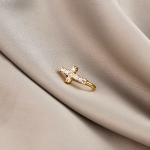 Macro detail of gold-plated cross ear cuff with micro-pave cubic zirconia on silk